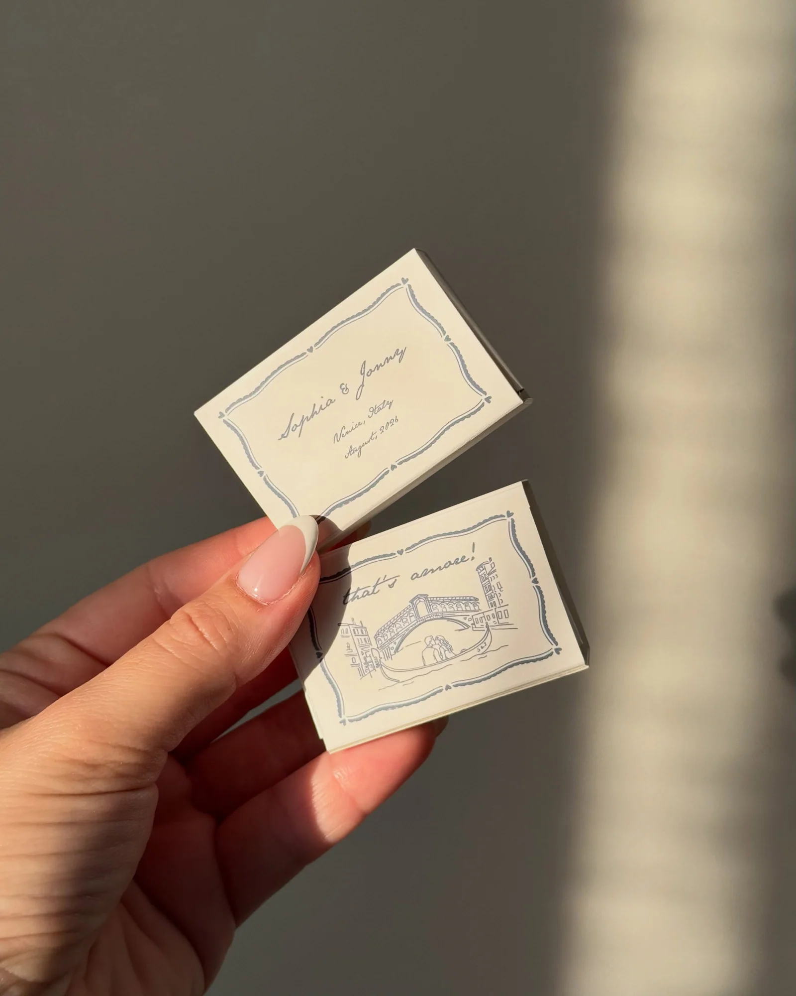 Ivory wedding matchboxes with a delicate blue Italian bridge illustration in warm sunlight
