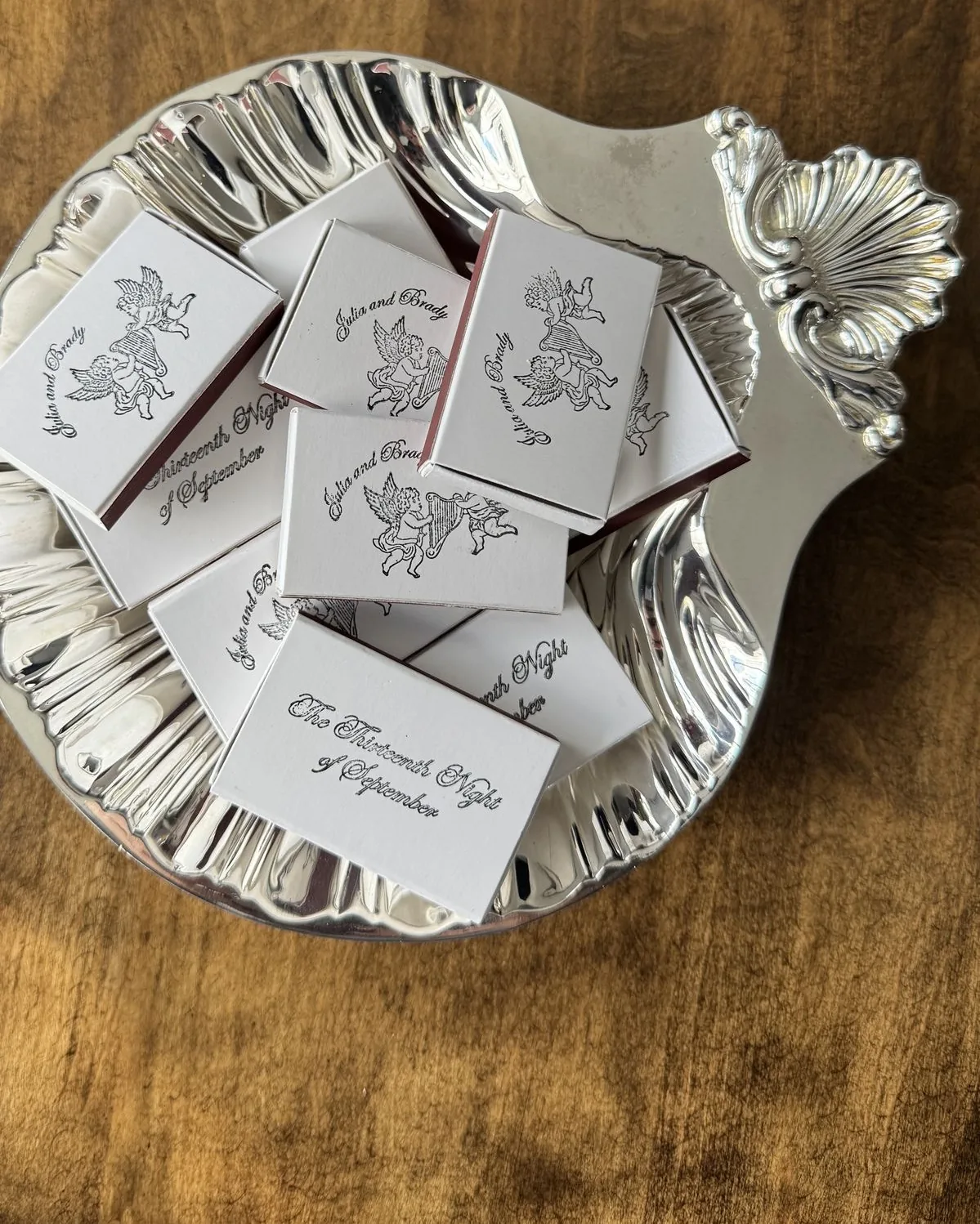 White matchboxes printed with cherubs and a date, piled on a silver shell dish