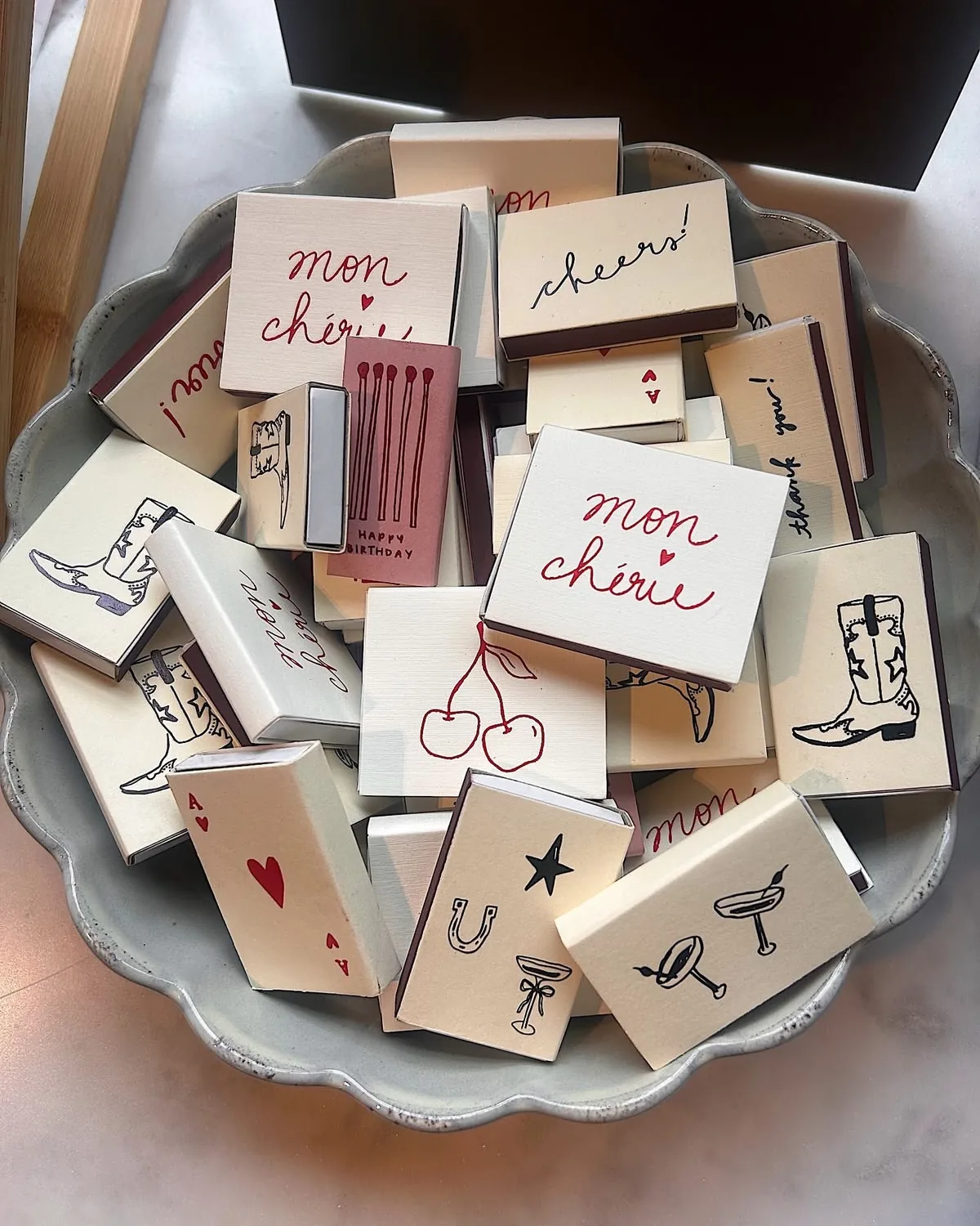 Cream matchboxes drawn with cherries, cowboy boots and the words mon chérie