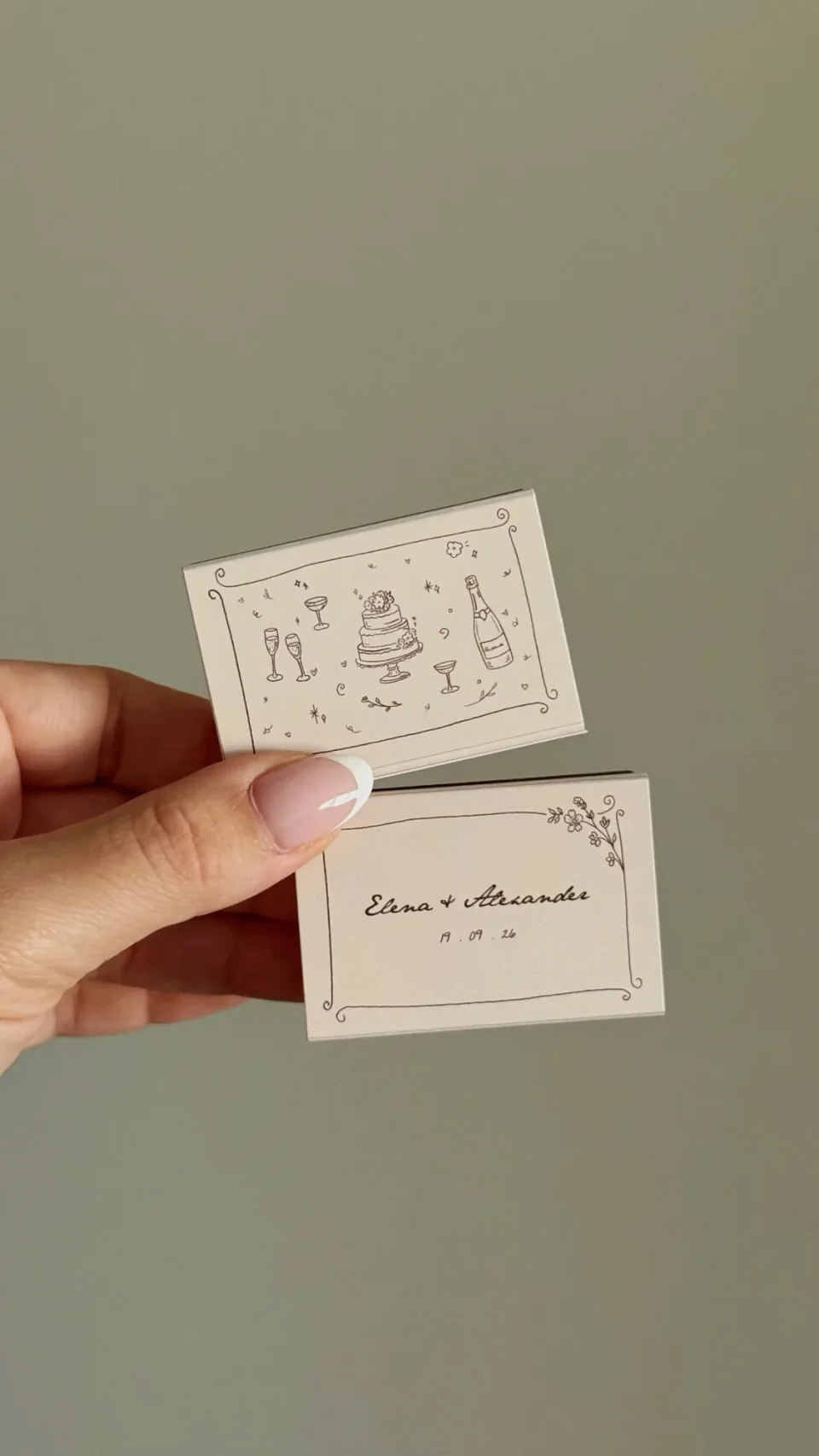 Pale matchboxes with a doodled cake, champagne and glasses, and two names with a date