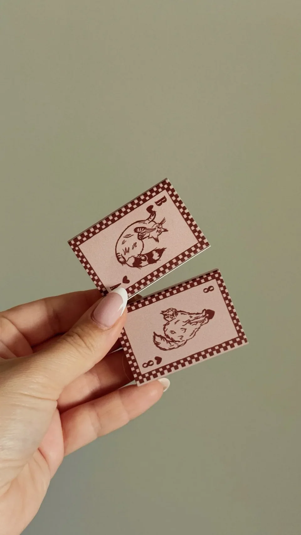 Pink matchboxes drawn as playing cards with two cats in a chequered border