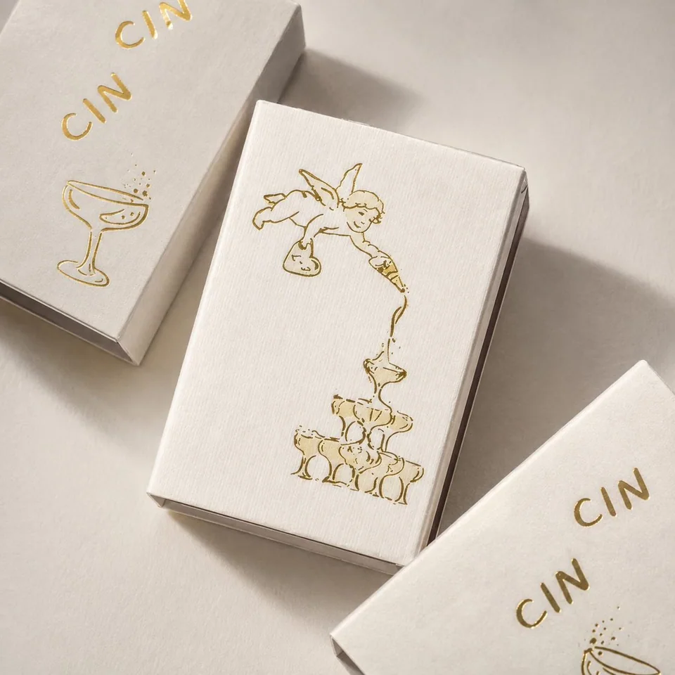 Cream matchboxes with gold foil drawings of a champagne tower
