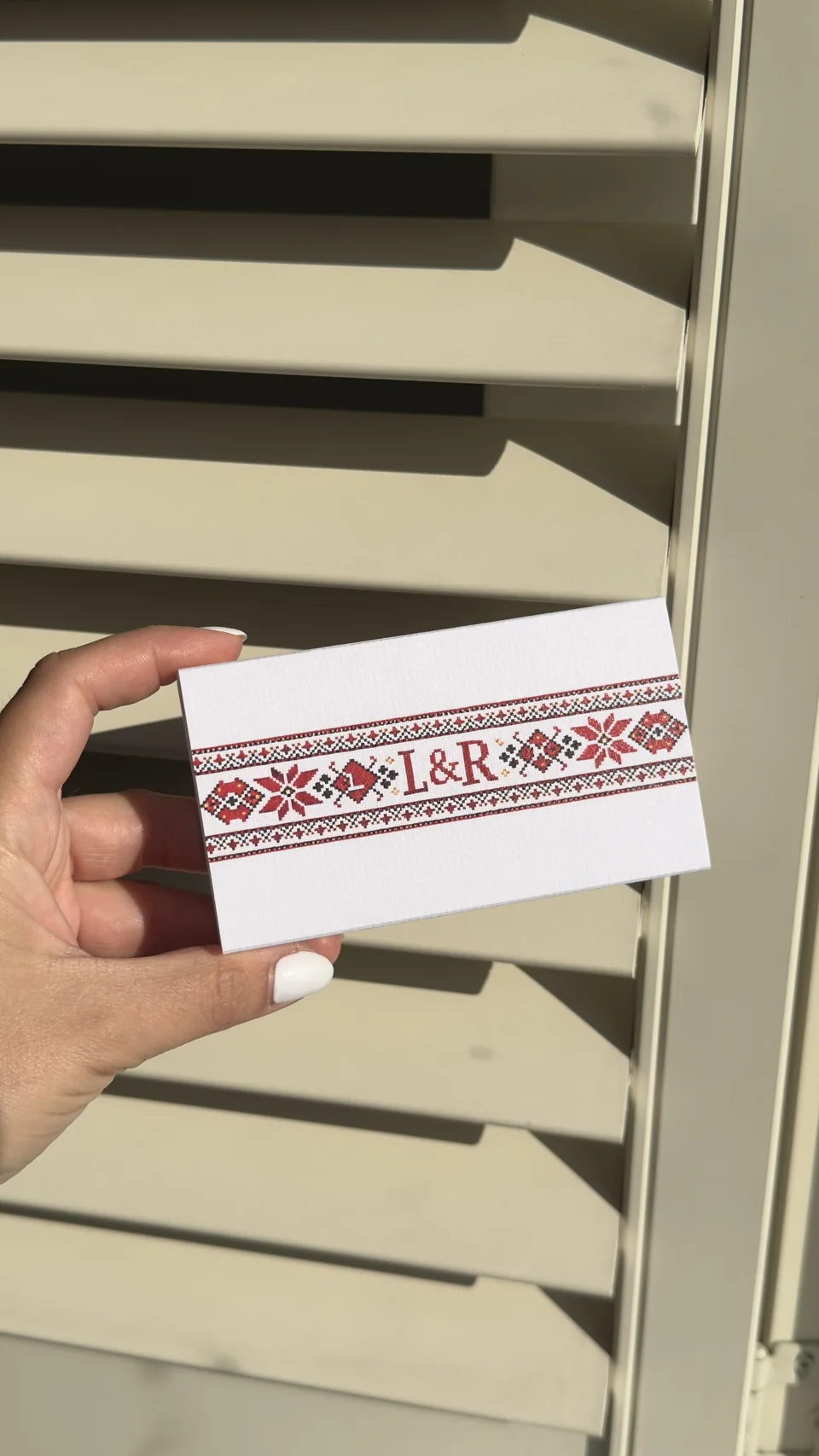 A large matchbox printed with a red cross-stitch band and the initials L and R