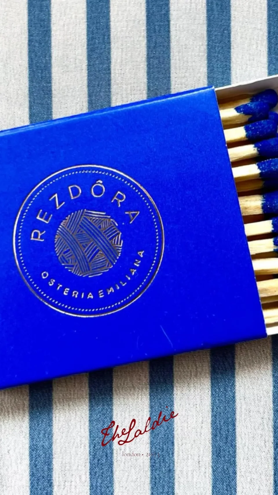 Cobalt blue Rezdôra matchbox with gold artwork on striped linen