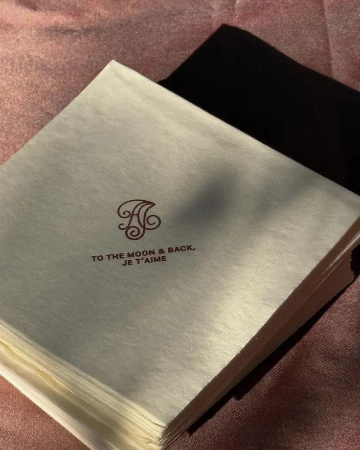 A stack of cream napkins printed with a red monogram and the words to the moon and back, je t’aime