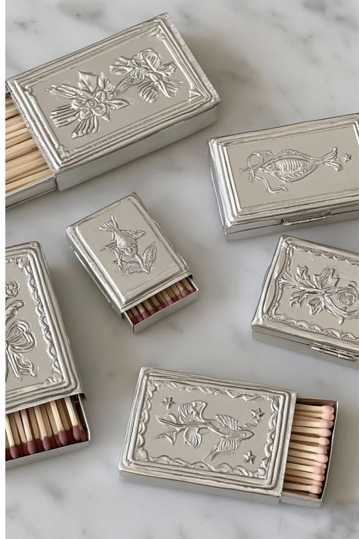 Silver matchboxes pressed with flowers, birds and fish, lying on marble with pink-tipped matches
